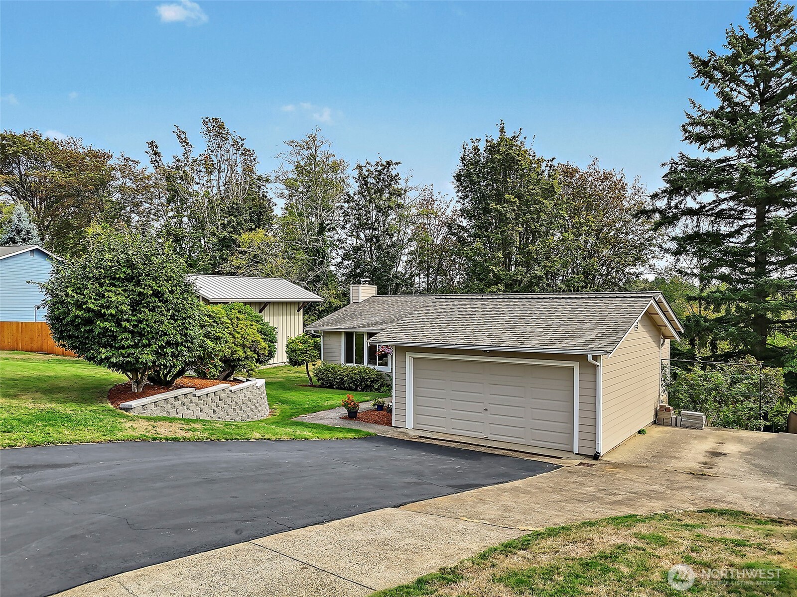 Home with a two-car garage, broad driveway, landscaped lawn, and mature trees.