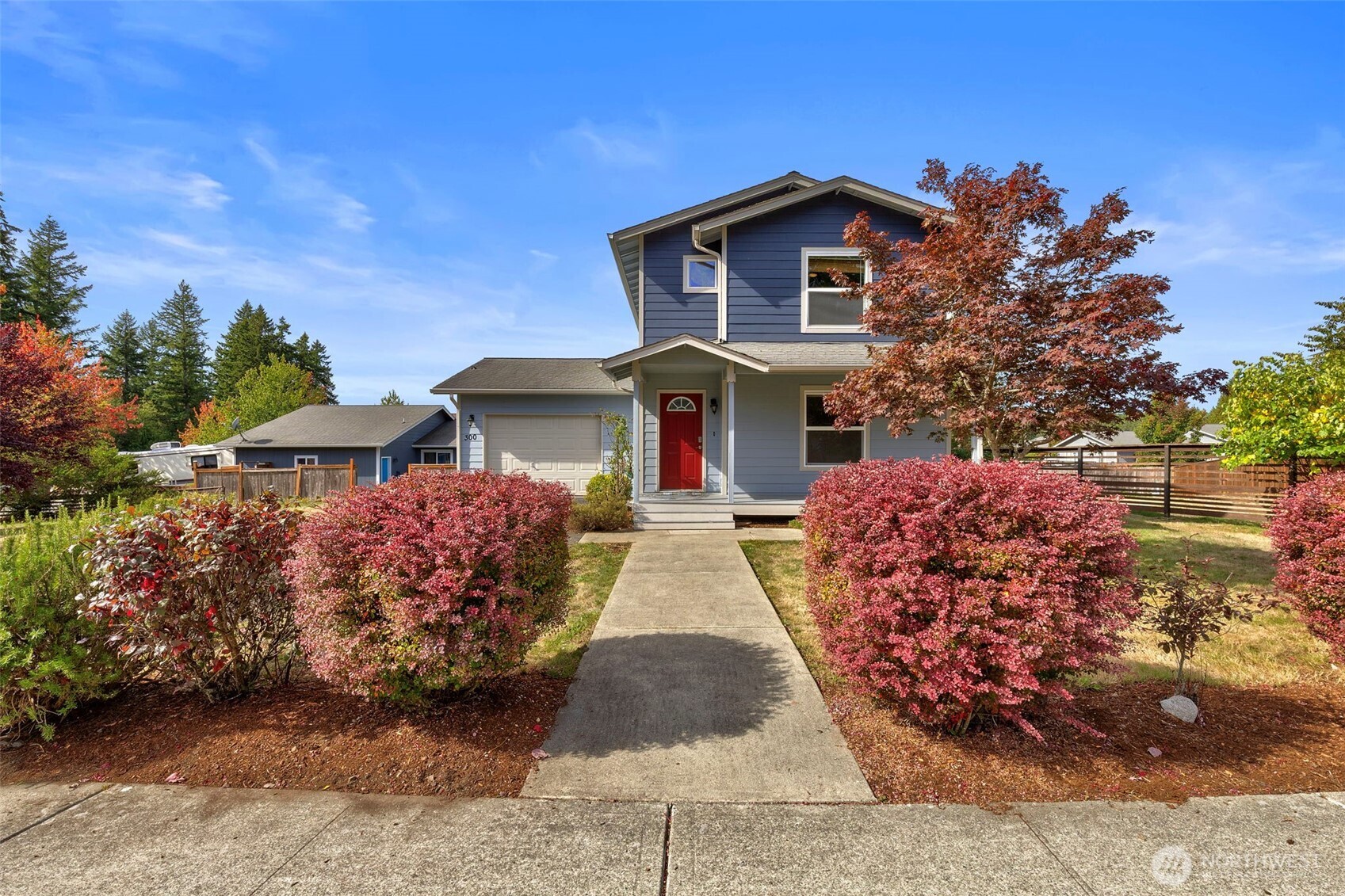 Blue two-story house with a red front door, attached garage, and colorful autumn landscaping.