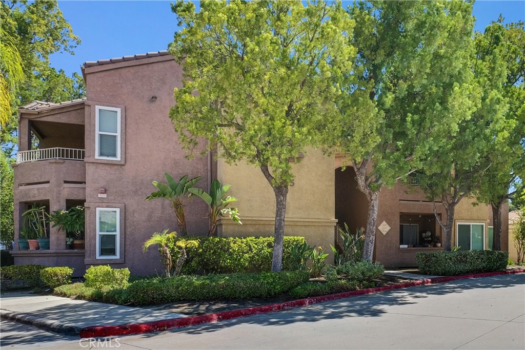 Two-story stucco building with balconies, mature trees, and landscaped frontage.