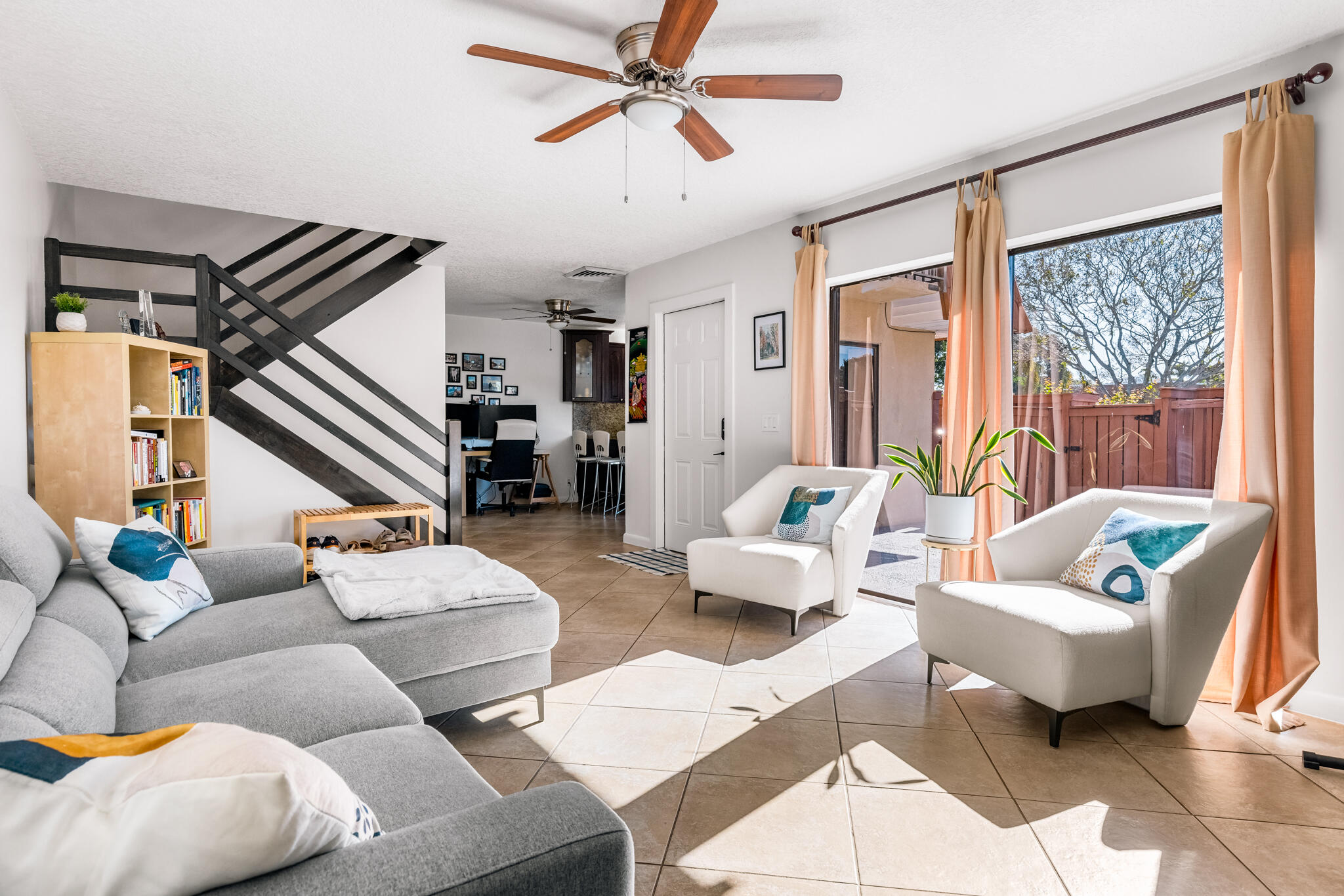 Living room with a gray sectional, white armchairs, and sliding doors opening to a fenced patio.
