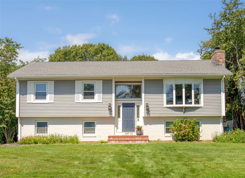 Split-level house with gray siding, white brick, a blue front door, and a broad lawn.