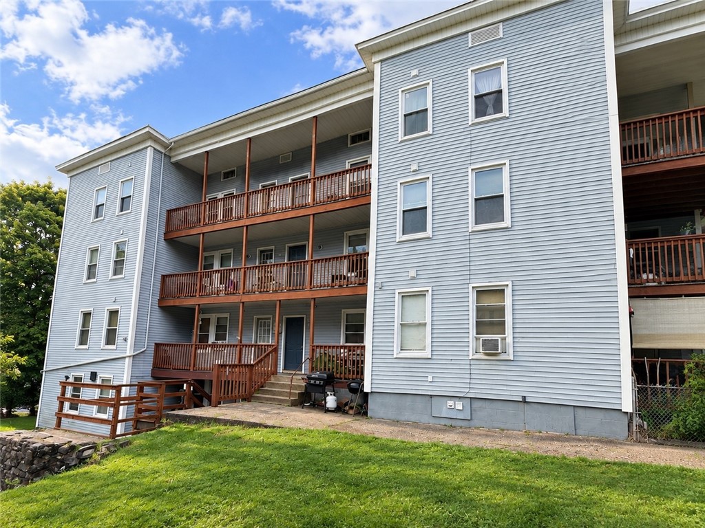 Blue-gray apartment building with three levels of wooden balconies and a grassy yard.