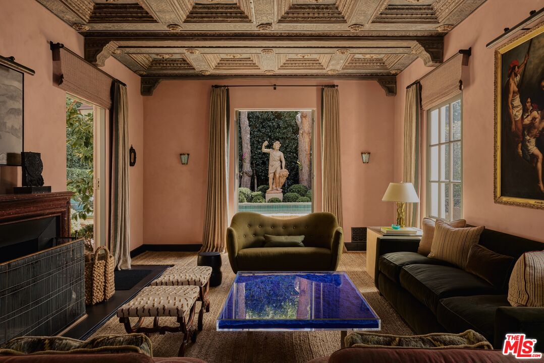 Living room with an ornate coffered ceiling, blue glass coffee table, and garden pool view.