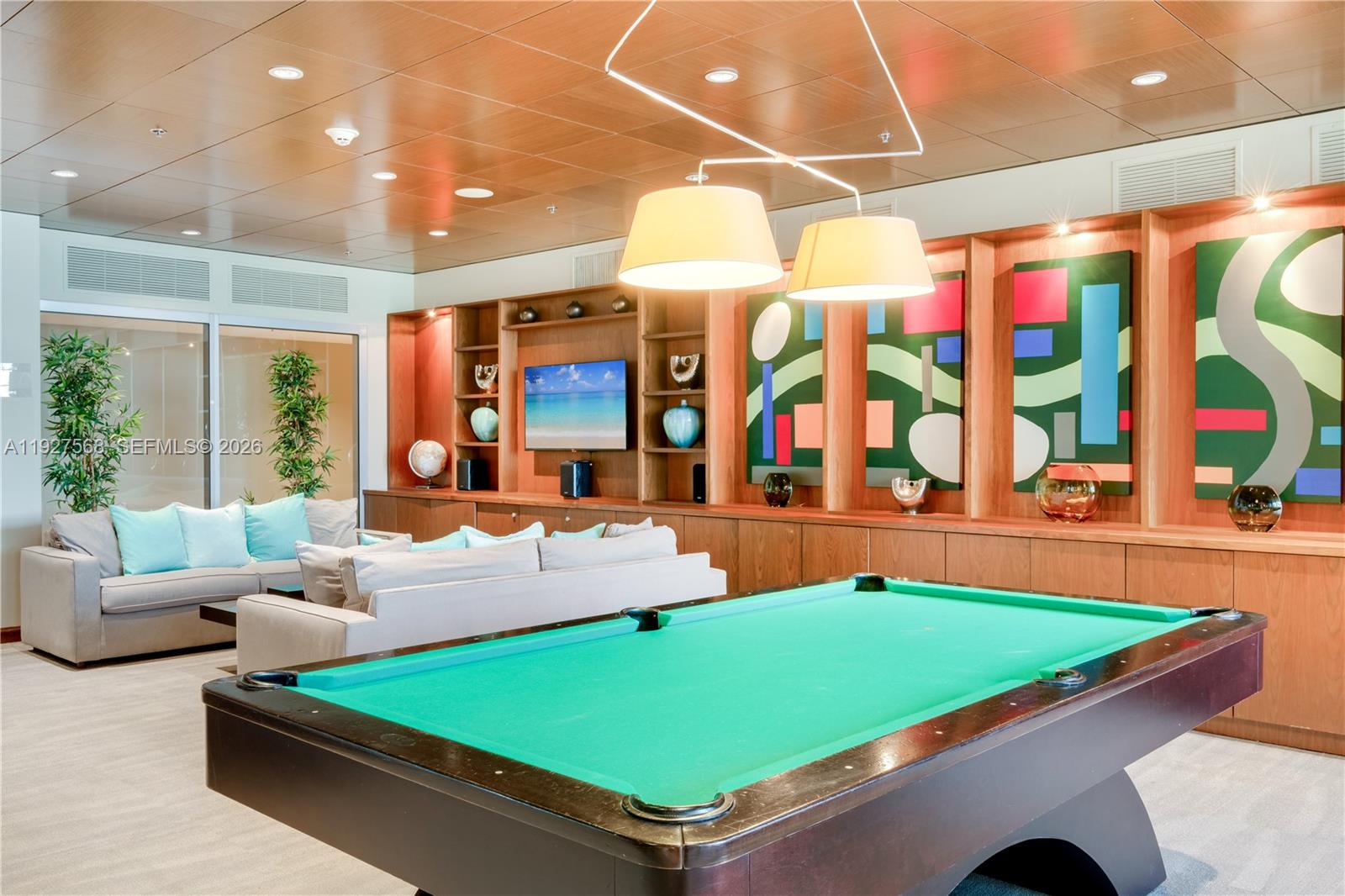 Billiards room with a green-felt pool table, pale sofas, and colorful abstract wall art.