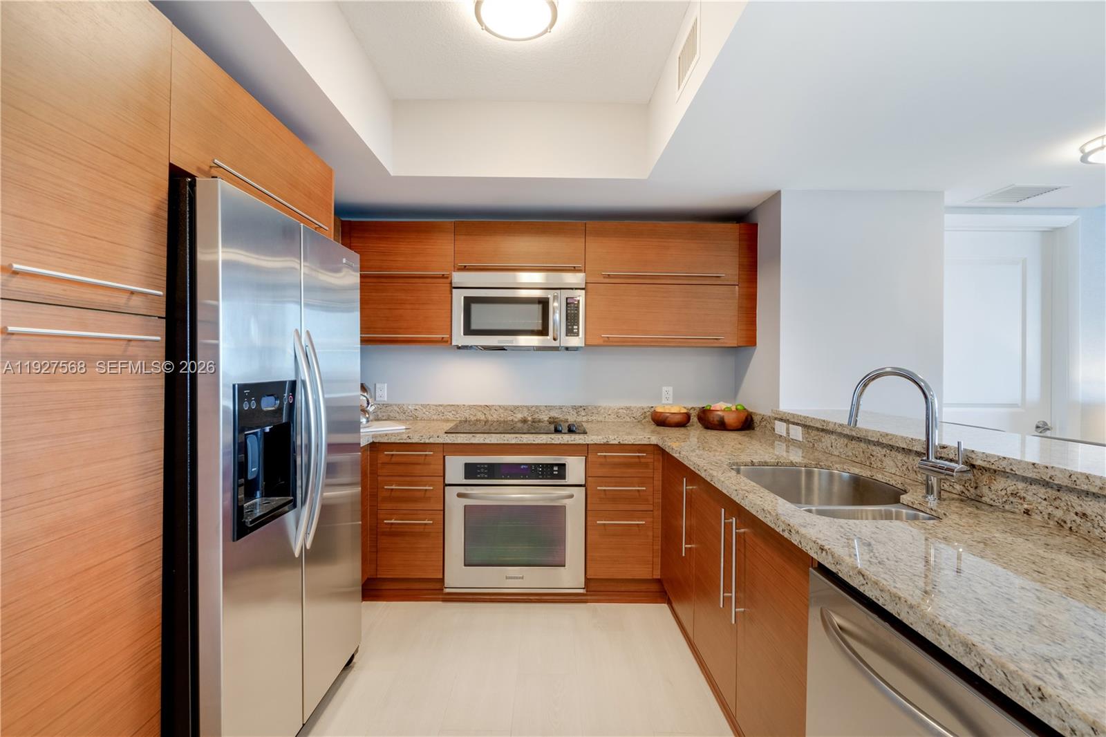 Modern kitchen with warm wood cabinetry, granite counters, stainless steel appliances, and a breakfast bar.