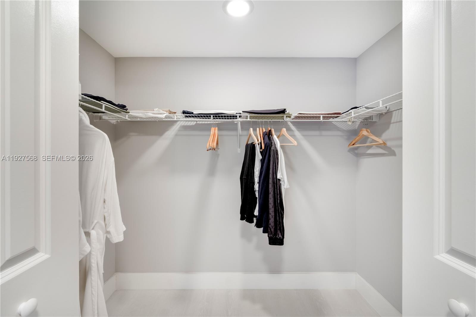 Walk-in closet with white wire shelving, folded clothes, wooden hangers, and a white robe.