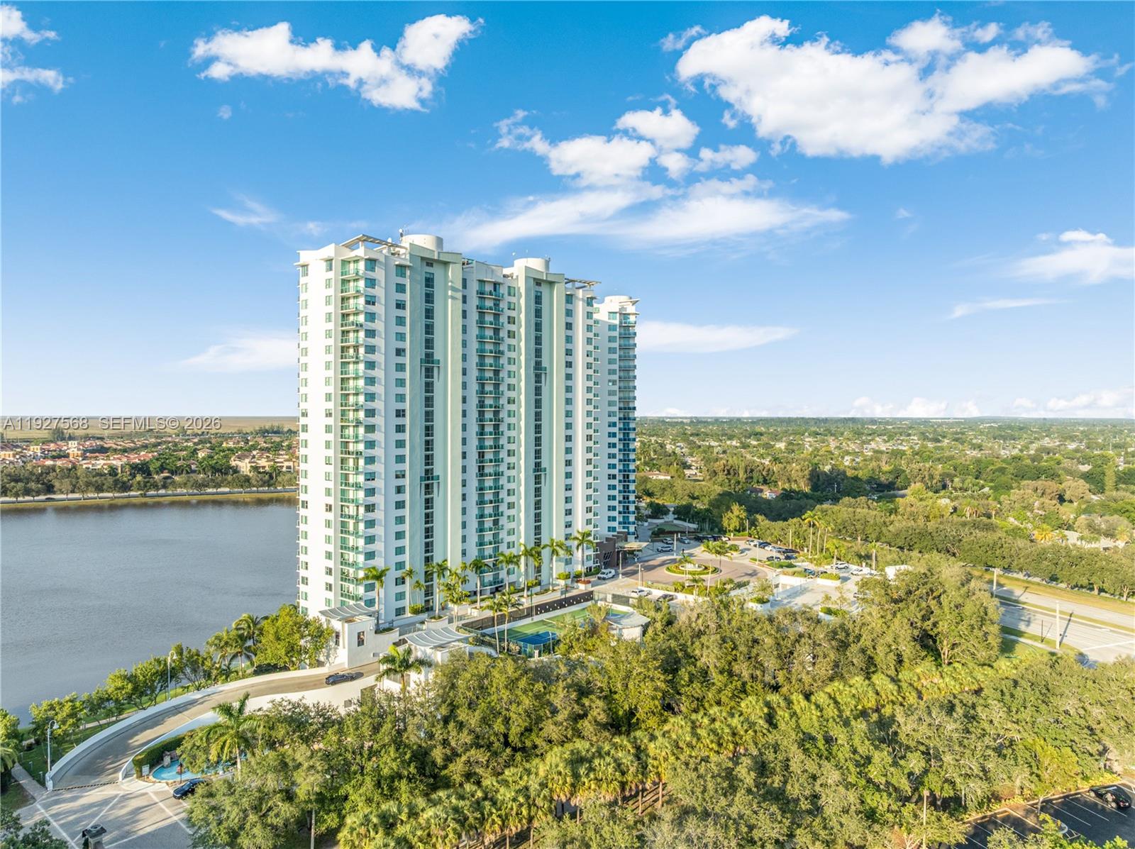 High-rise condominium beside a lake, with landscaped grounds and a pool.