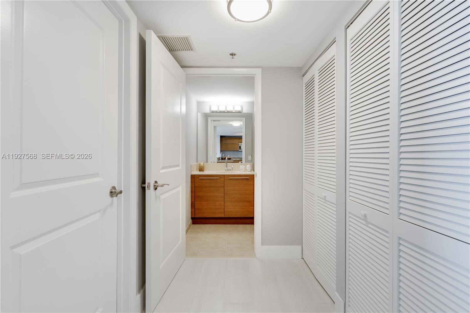 Hallway leading to a bathroom vanity, with white louvered closet doors along the right wall.