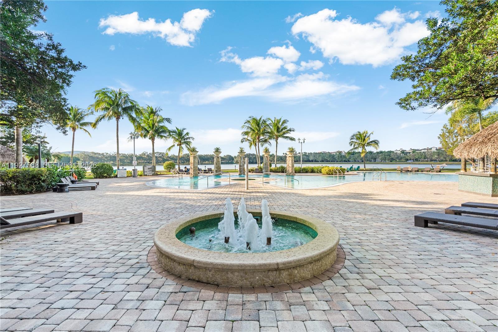 Resort-style pool courtyard with a central fountain, palm trees, and lakeside views.