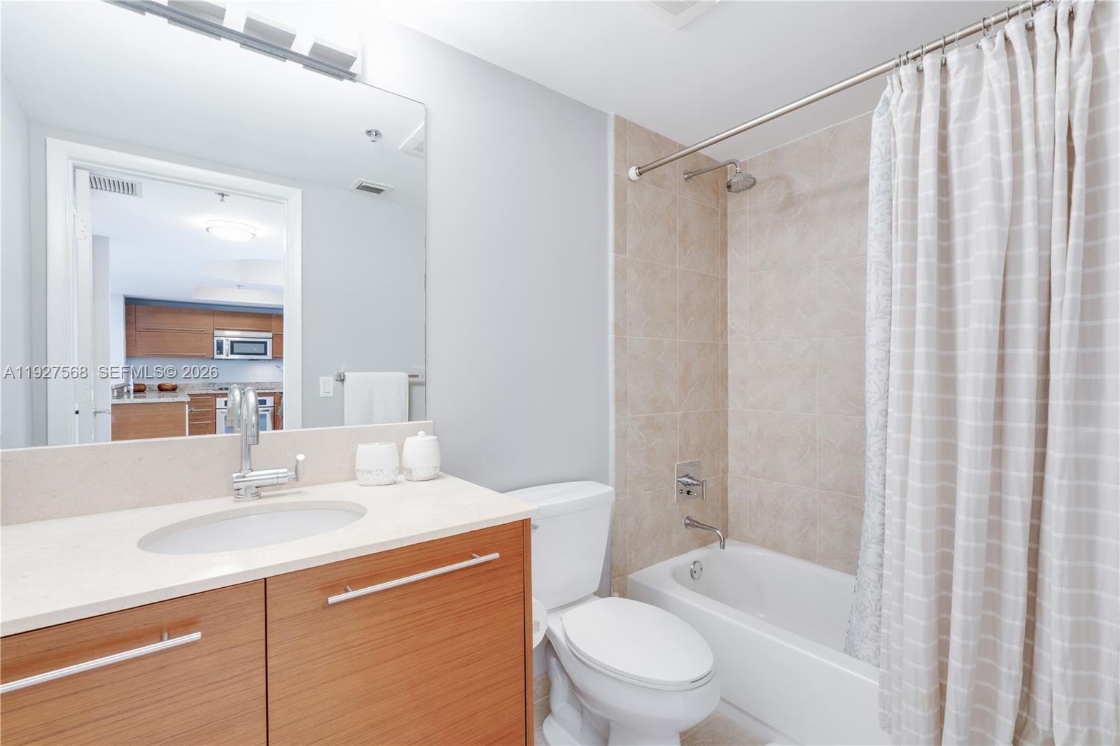 Bathroom with a wood-front vanity, large mirror, and tiled bathtub-shower.