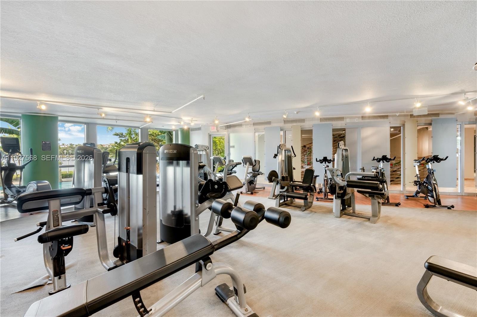 Fitness room with weight machines and stationary bikes beside large windows.