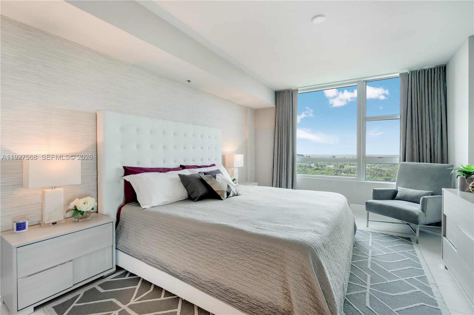 Furnished bedroom with an upholstered bed and tall windows overlooking greenery.