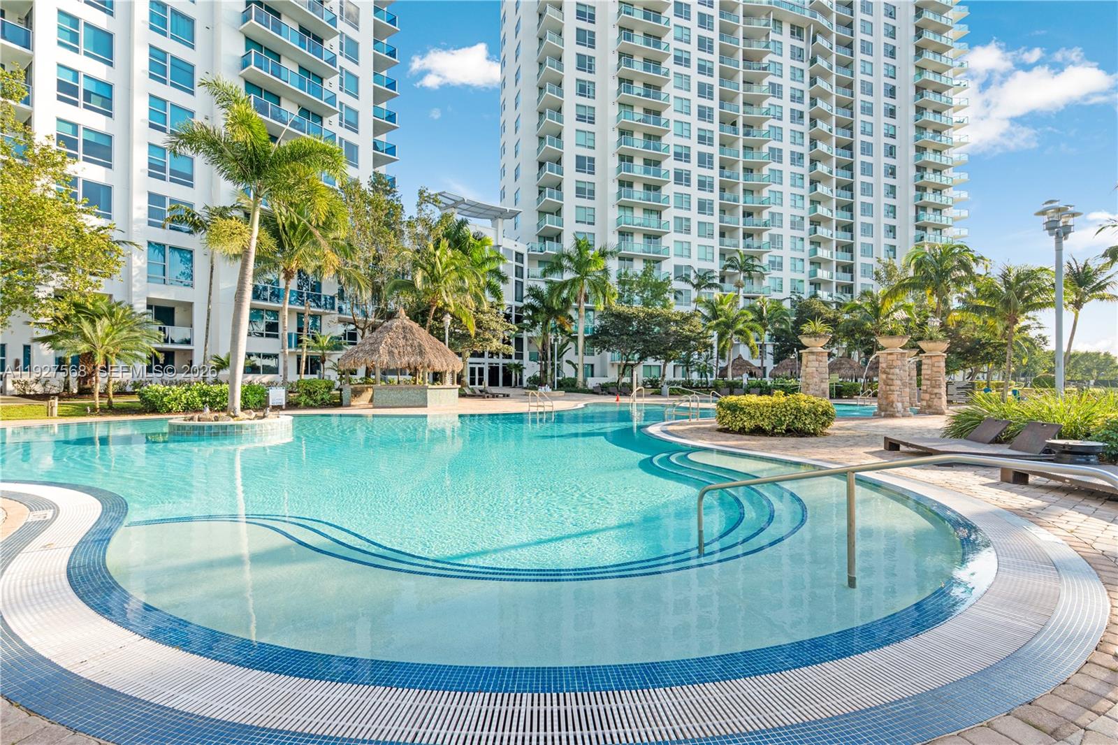High-rise condominium beside a curved pool, with palm trees and a thatched cabana.