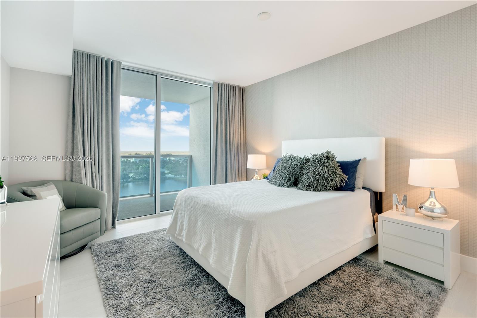 Bedroom with a white bed and balcony doors overlooking water.