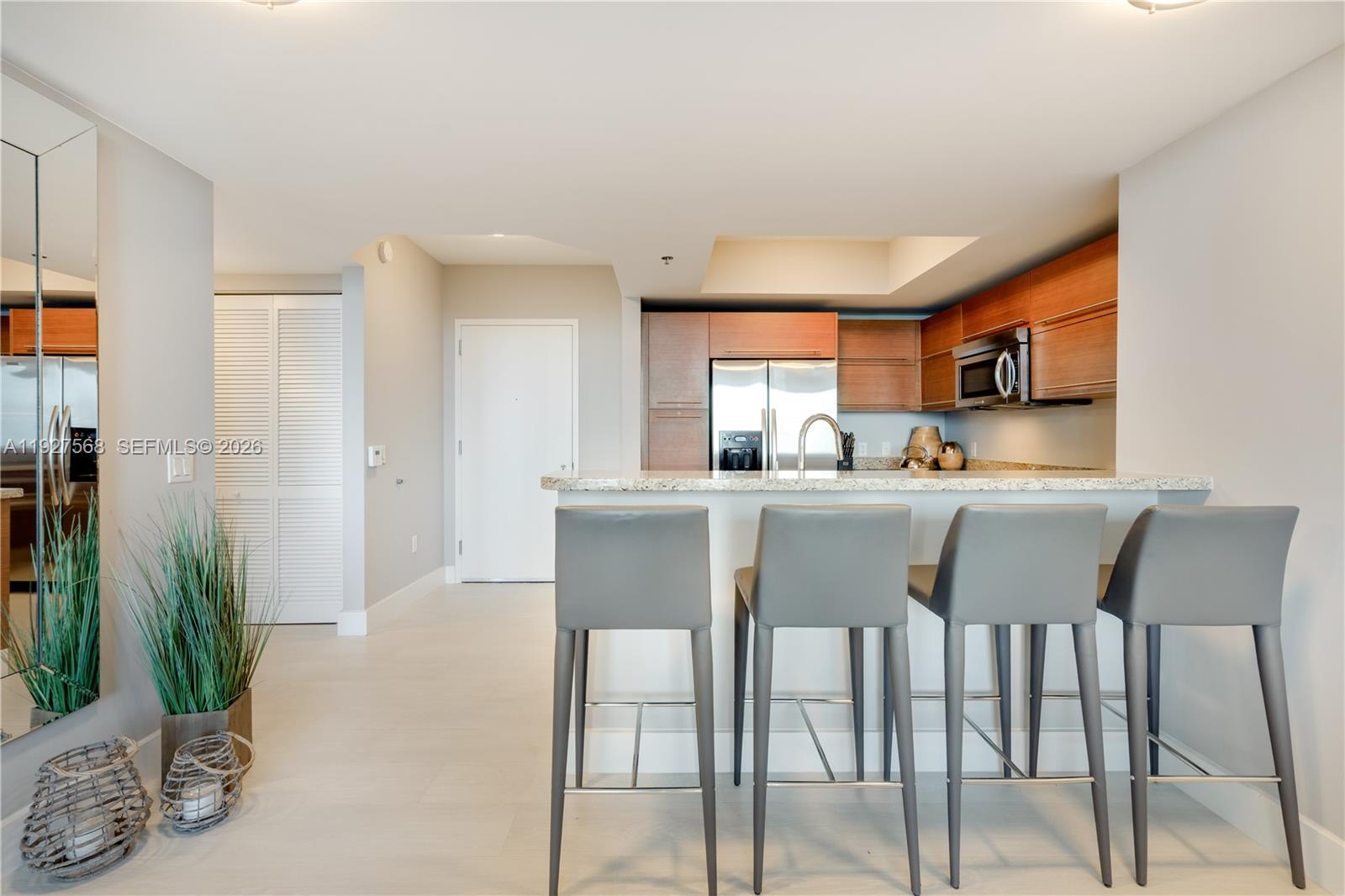 Open kitchen with wood cabinets, stainless steel appliances, and a granite breakfast bar with four gray stools.