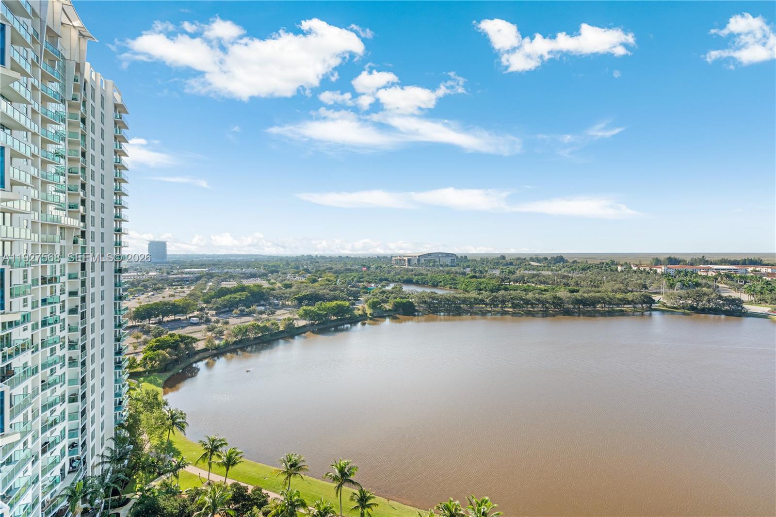 High-rise condominium beside a lake, with landscaped grounds and a distant city view.