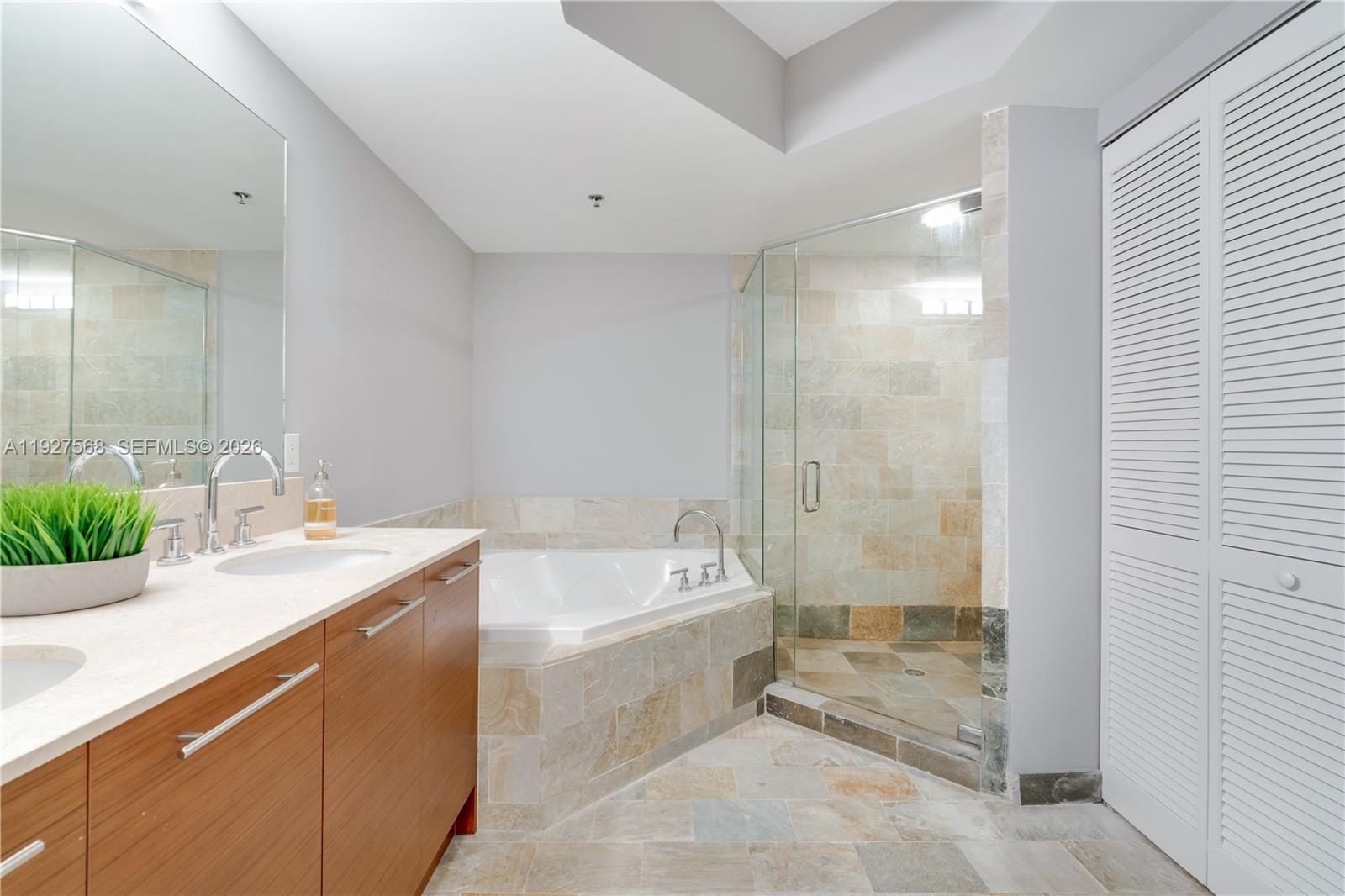 Bathroom with a stone-tiled soaking tub, glass shower, and wood-front vanity.