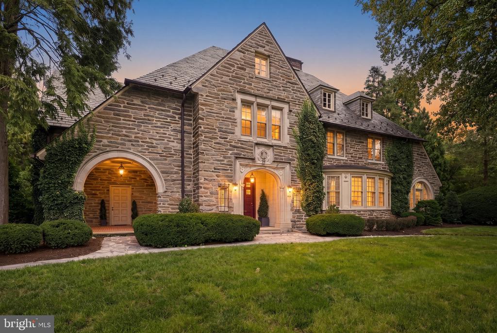 1926 Normandy stone estate front exterior illuminated at dusk with arched stone portico and landscaped front lawn at 1199 Reading Boulevard.