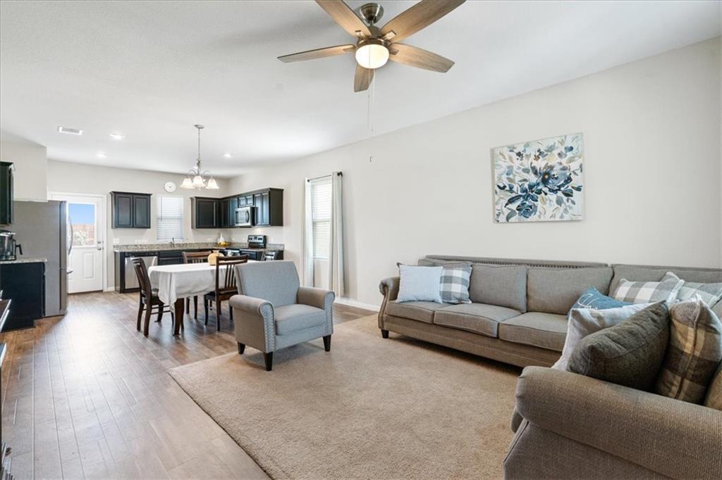 Open-plan living room with gray sectional, ceiling fan, and dining area beside a dark-cabinet kitchen.
