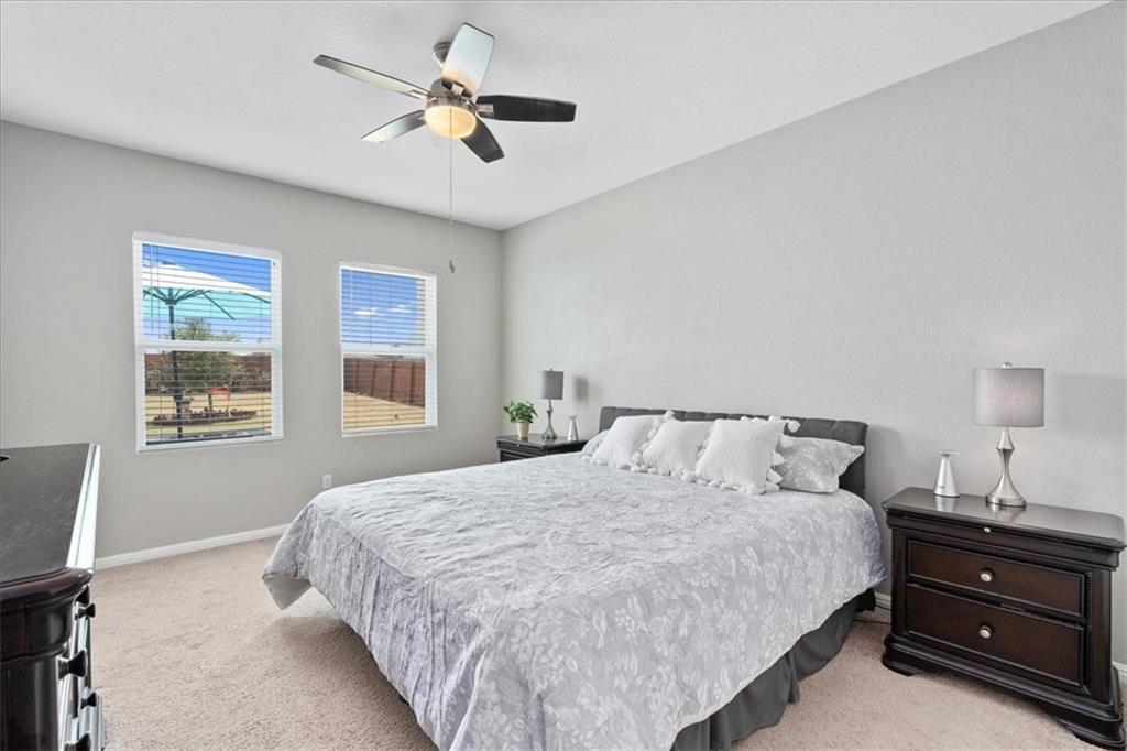 Bedroom with pale patterned bedding, two windows, a ceiling fan, and dark wood nightstands.