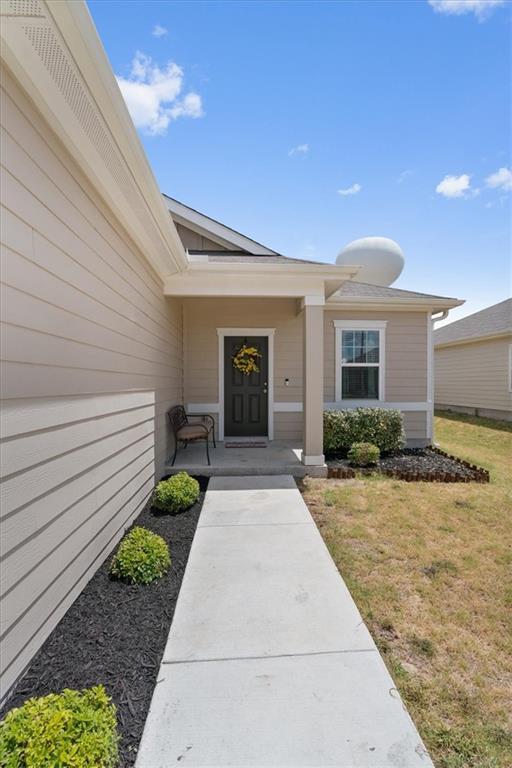 Home entrance with a covered porch, wreath on the front door, and concrete walkway.