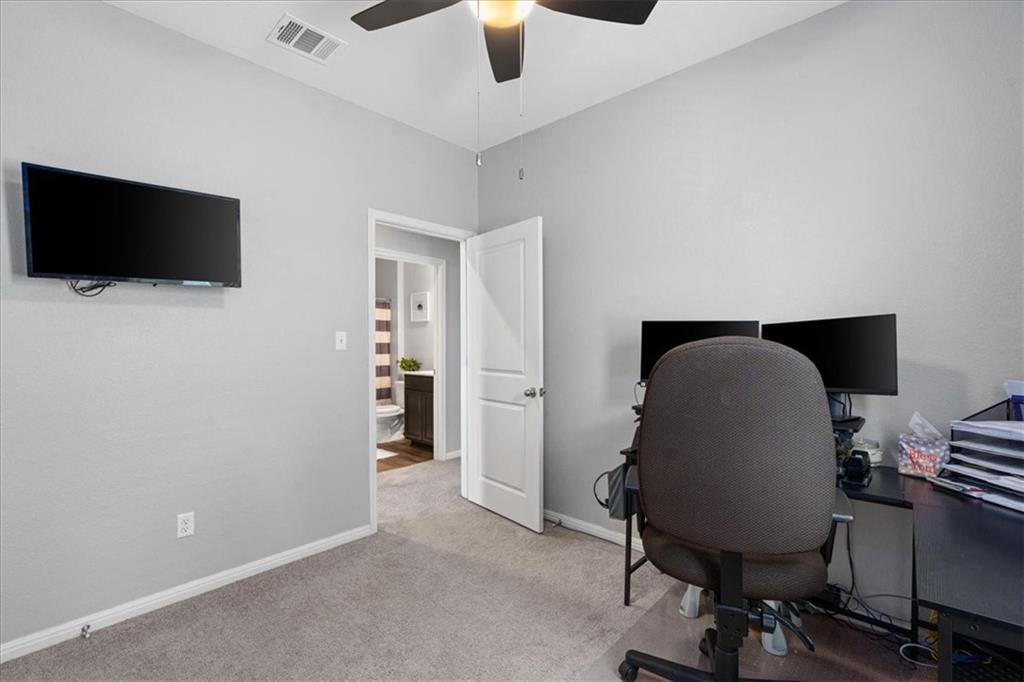 Furnished home office with a wall-mounted TV and dual-monitor desk beside an open bathroom doorway.