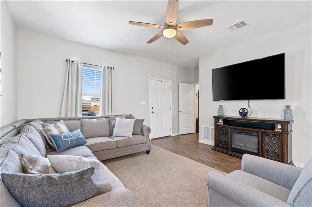 Living room with a gray sectional, wall-mounted TV, dark wood fireplace console, and ceiling fan.