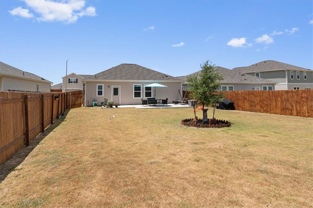 Home viewed across a fenced backyard with a patio umbrella and a young tree.