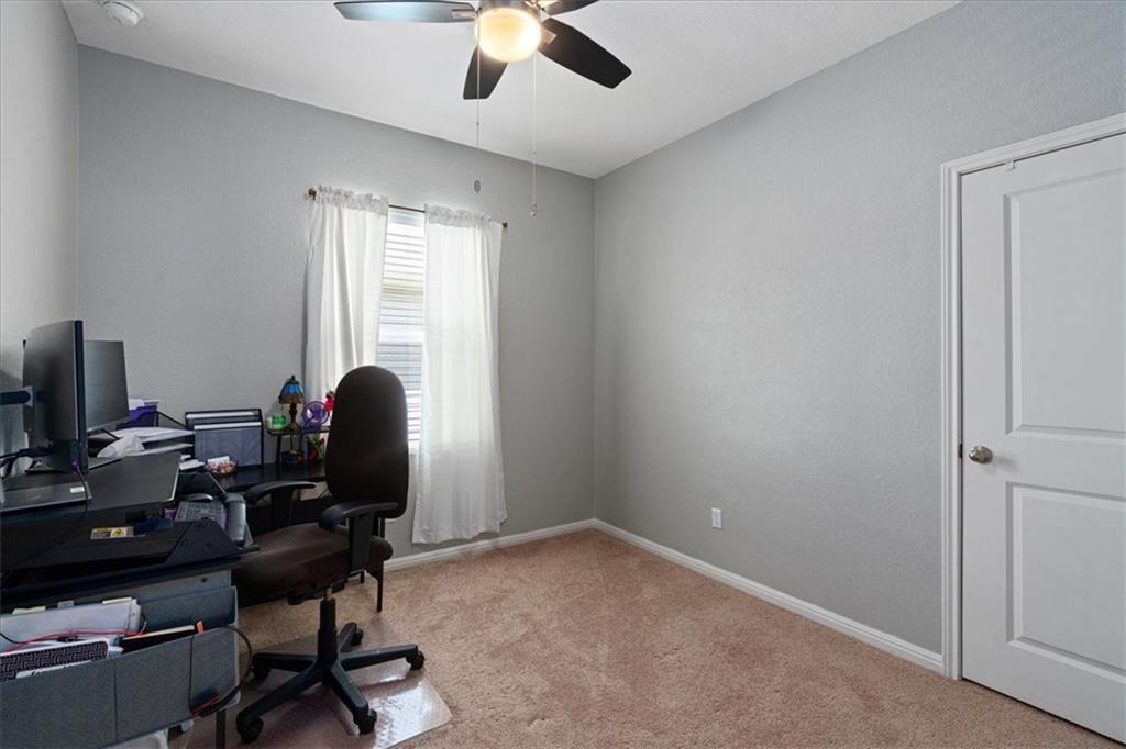 Carpeted bedroom office with a desk and computer beside a curtained window and ceiling fan.