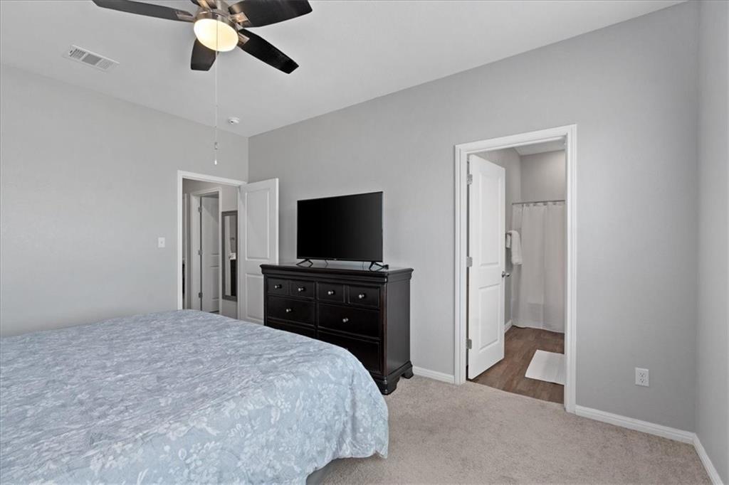 Bedroom with a patterned bedspread, dark dresser and television, and open bathroom doorway.