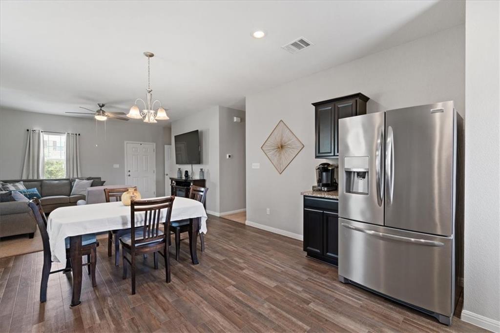Open kitchen and dining area with a stainless refrigerator and wood-look floors, adjoining the living room.