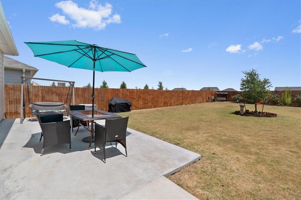 Backyard patio with turquoise umbrella and wicker seating beside a fenced lawn.