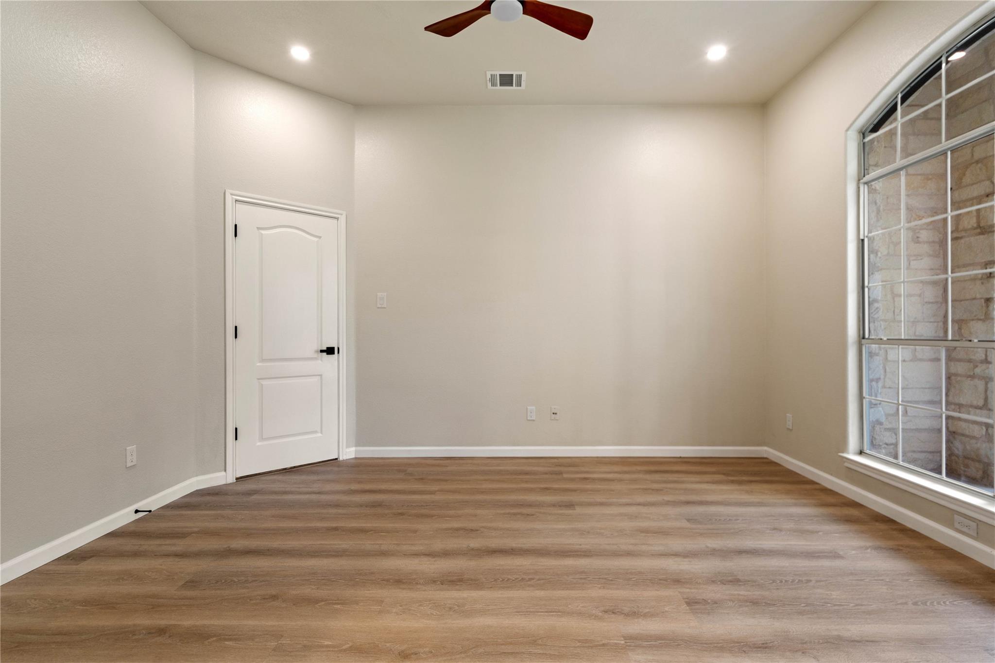 Empty room with wood-look flooring, a ceiling fan, and a large window.
