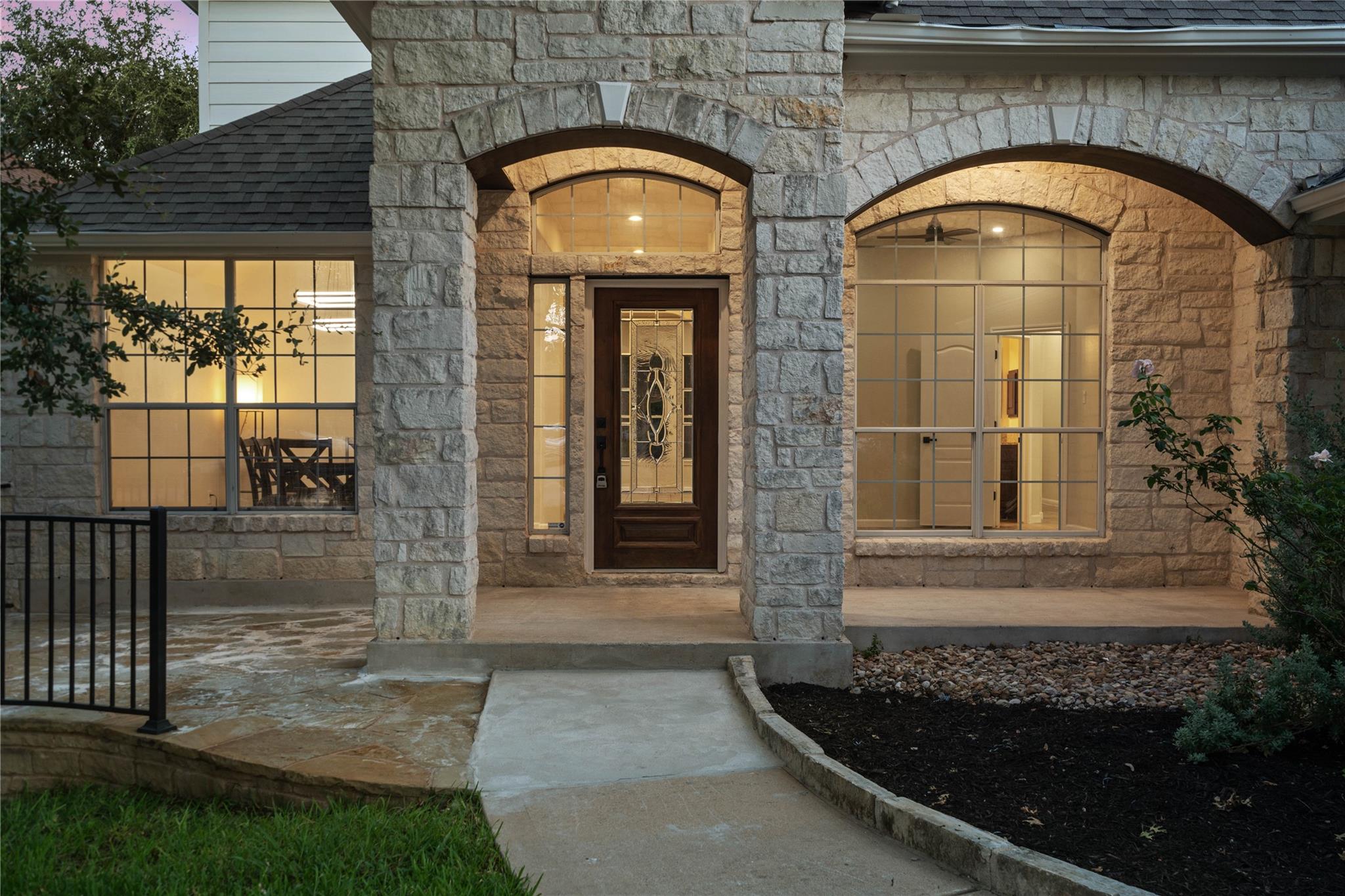 Stone home entrance with arched windows, a decorative glass door, and warm evening lighting.