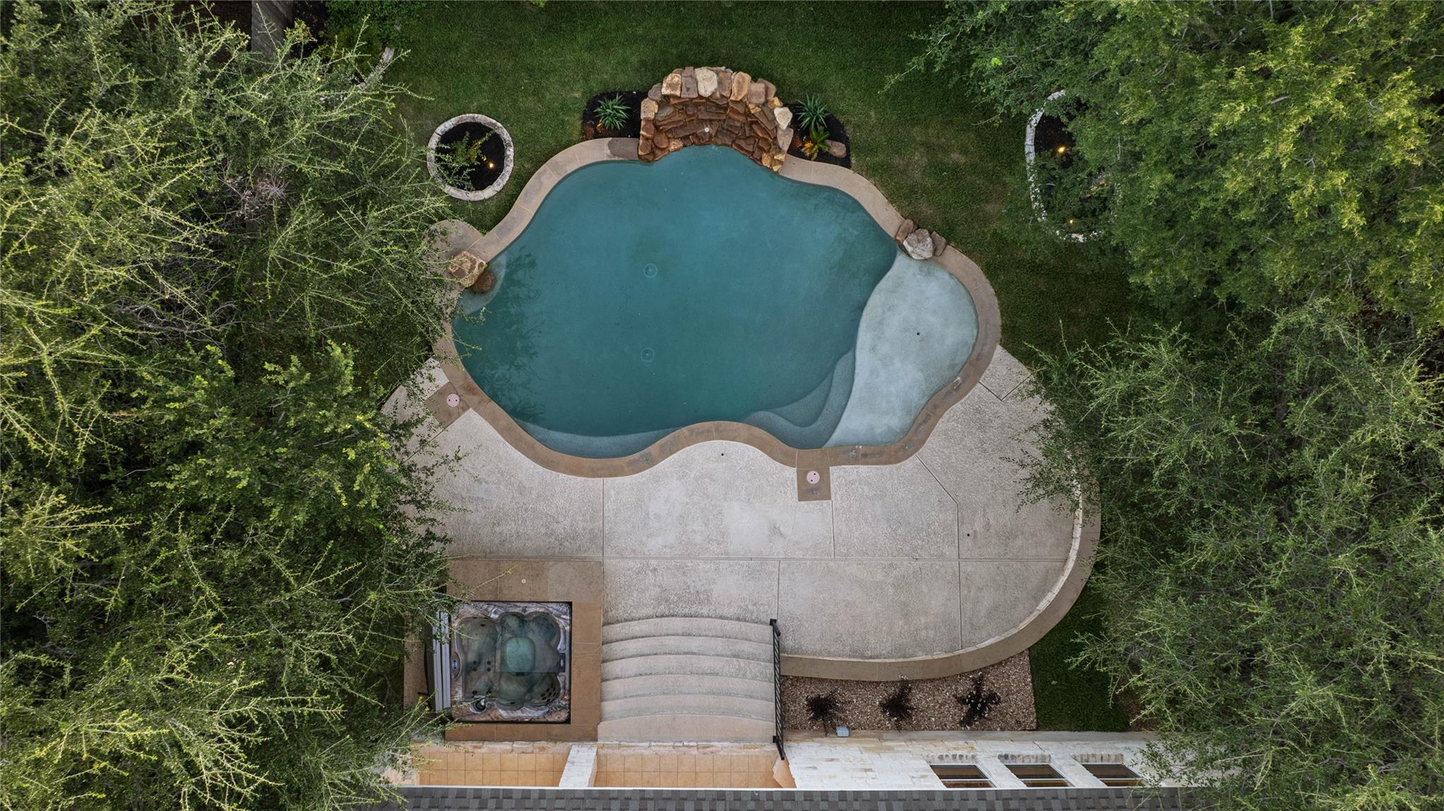 Aerial view of a freeform backyard pool with rock waterfall, spa, and surrounding trees.