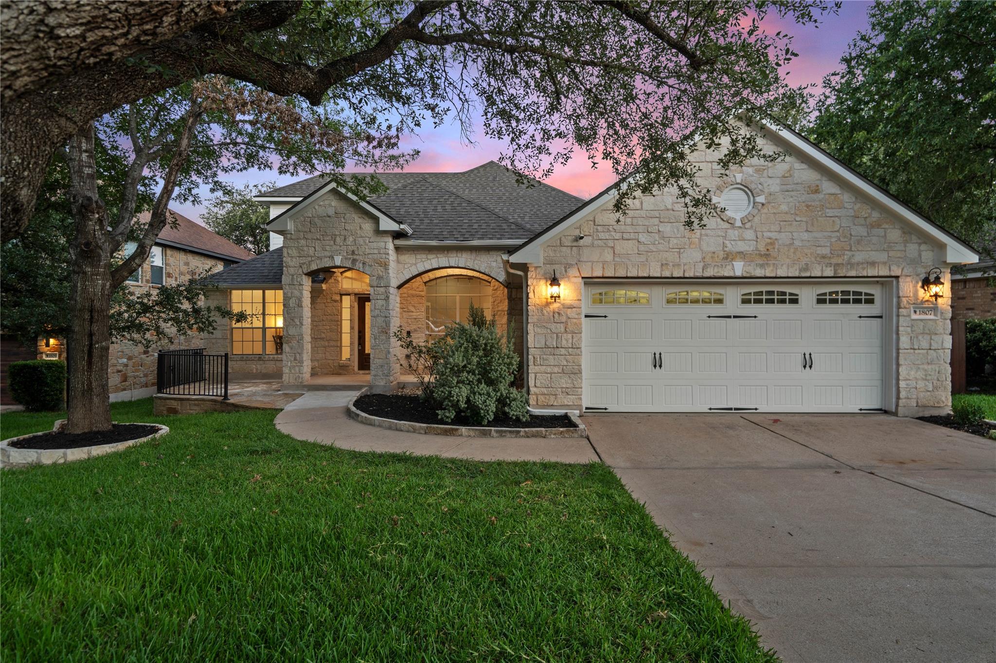 Stone-front home with arched entry and two-car garage at dusk.