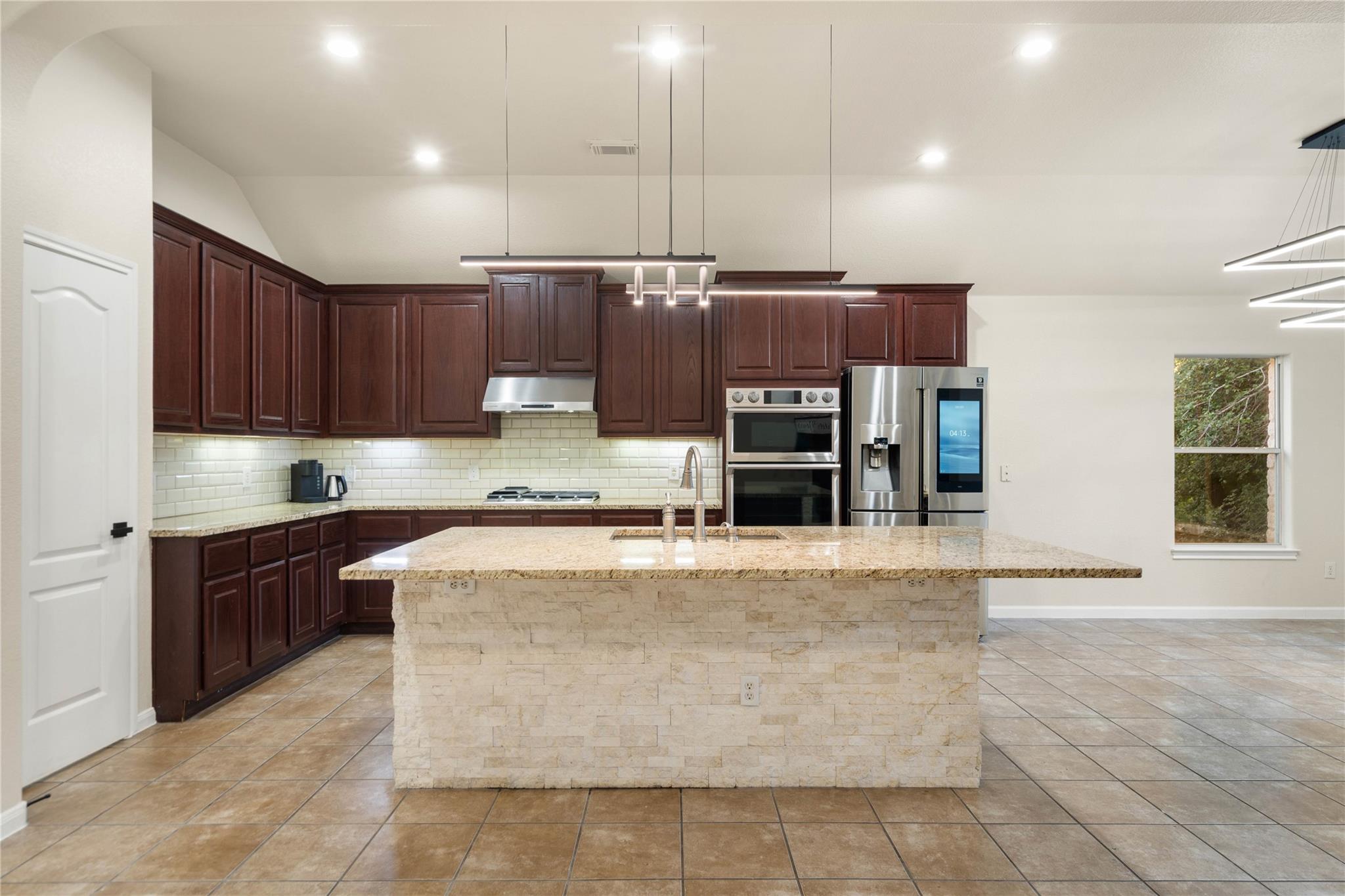 Kitchen with dark wood cabinets, a stone island, stainless appliances, and tile flooring.