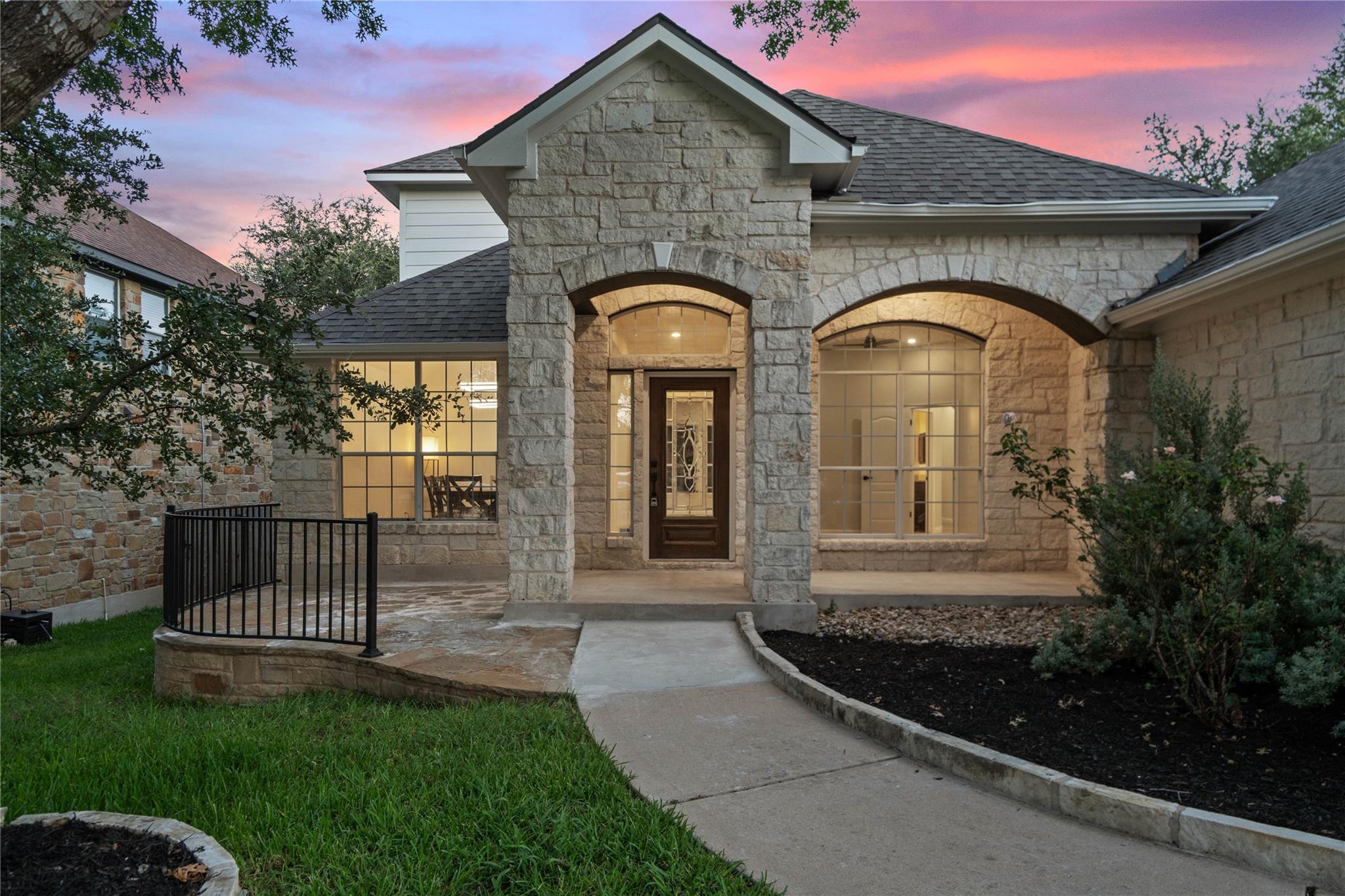 Stone-front home with arched entry and windows, warmly lit beneath a pink dusk sky.