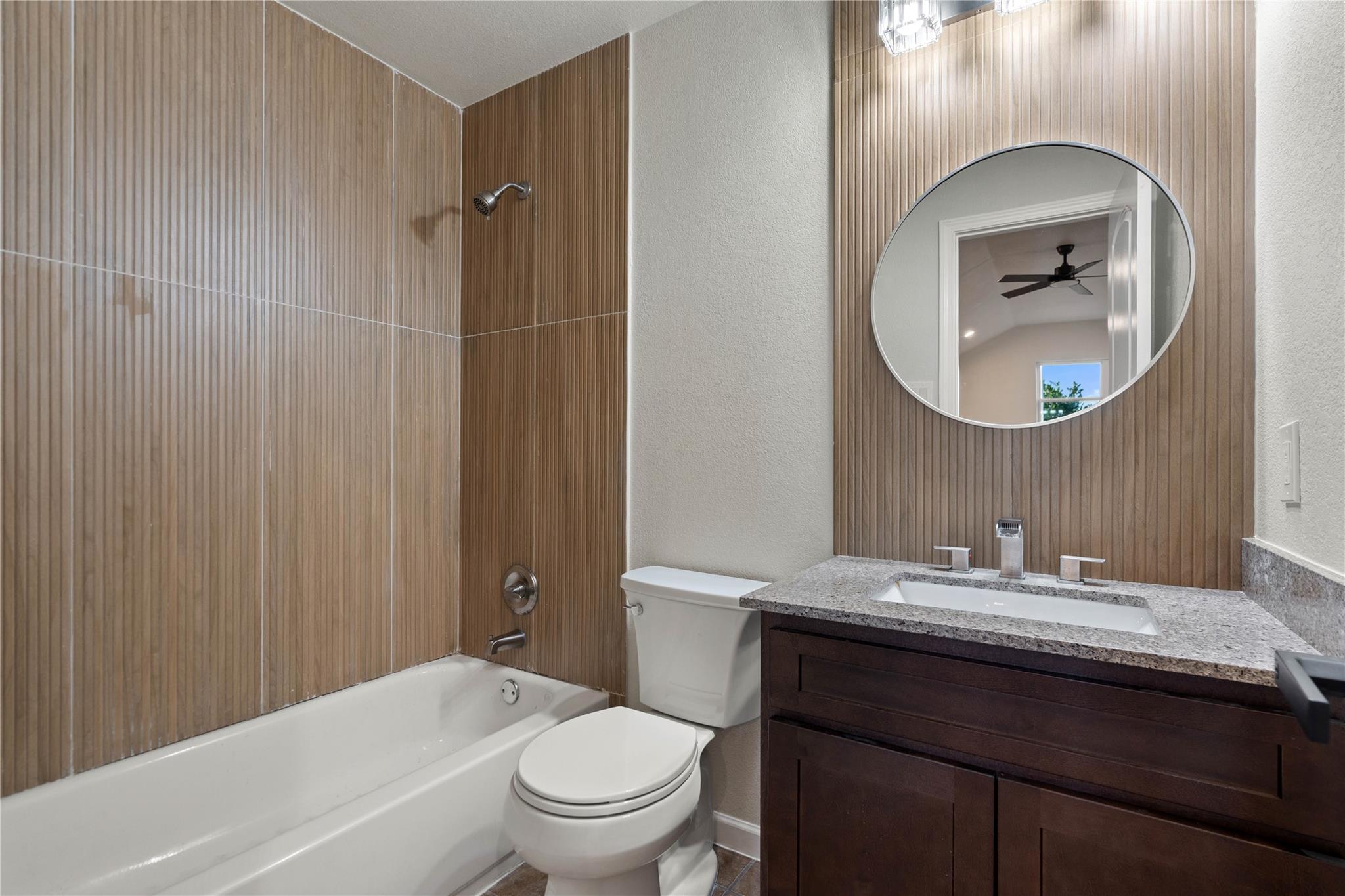 Bathroom with a tub-shower, wood-look tile, dark vanity, and round mirror.