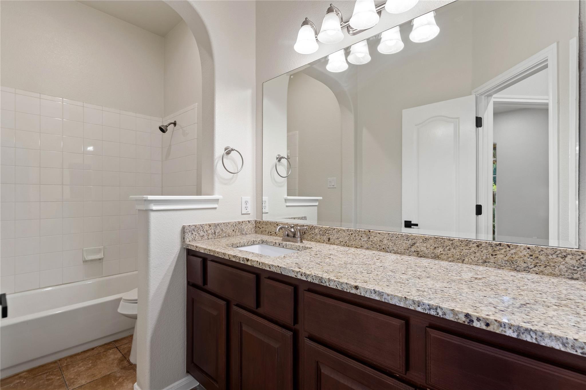 Bathroom with a granite vanity, dark wood cabinets, and a tiled tub and shower.