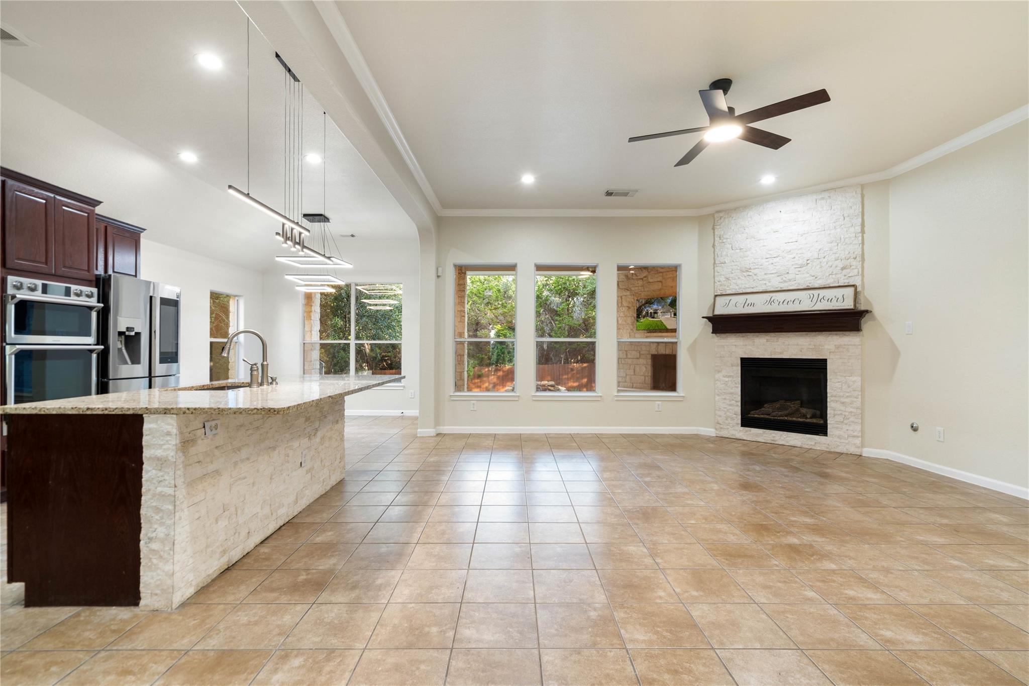 Open kitchen and living area with a stone island, tiled floors, and a white stone fireplace.