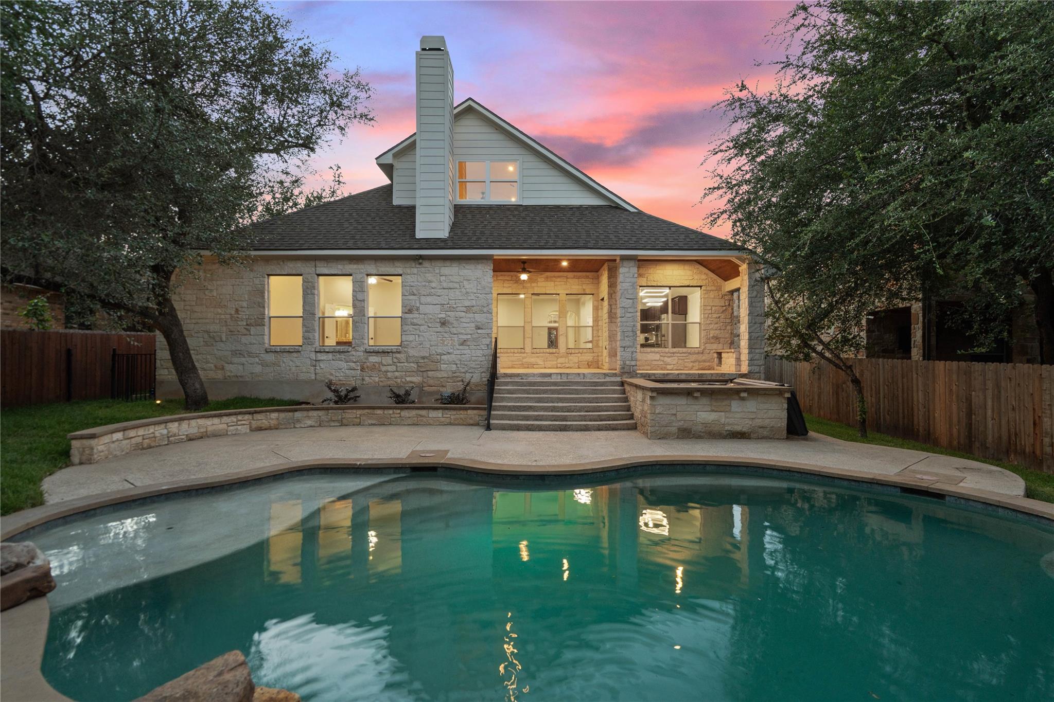 Stone house and backyard pool beneath a vivid pink sunset sky.