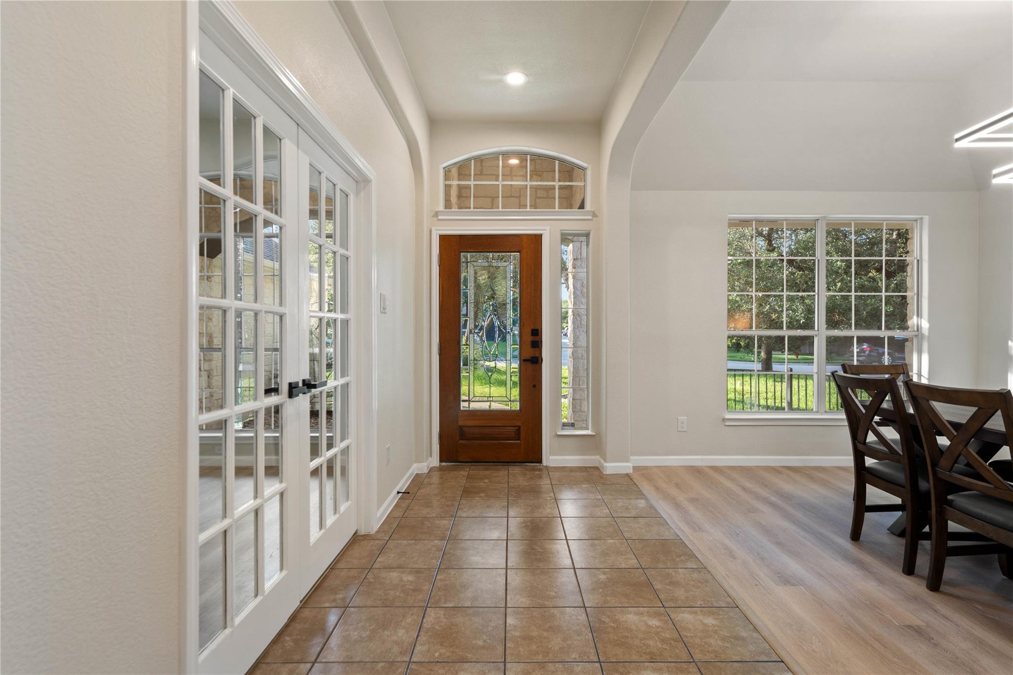 Entryway with a wood-and-glass front door, tiled floor, and dining table beside a large window.