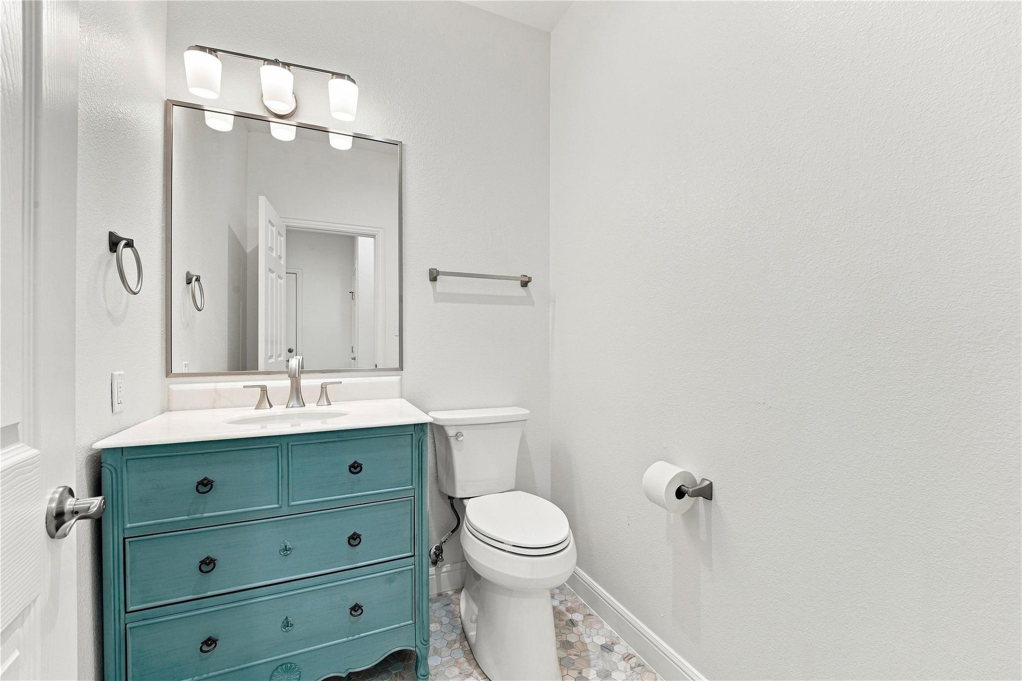 Bathroom with a teal-blue vanity, framed mirror, white toilet, and hexagonal tile floor.
