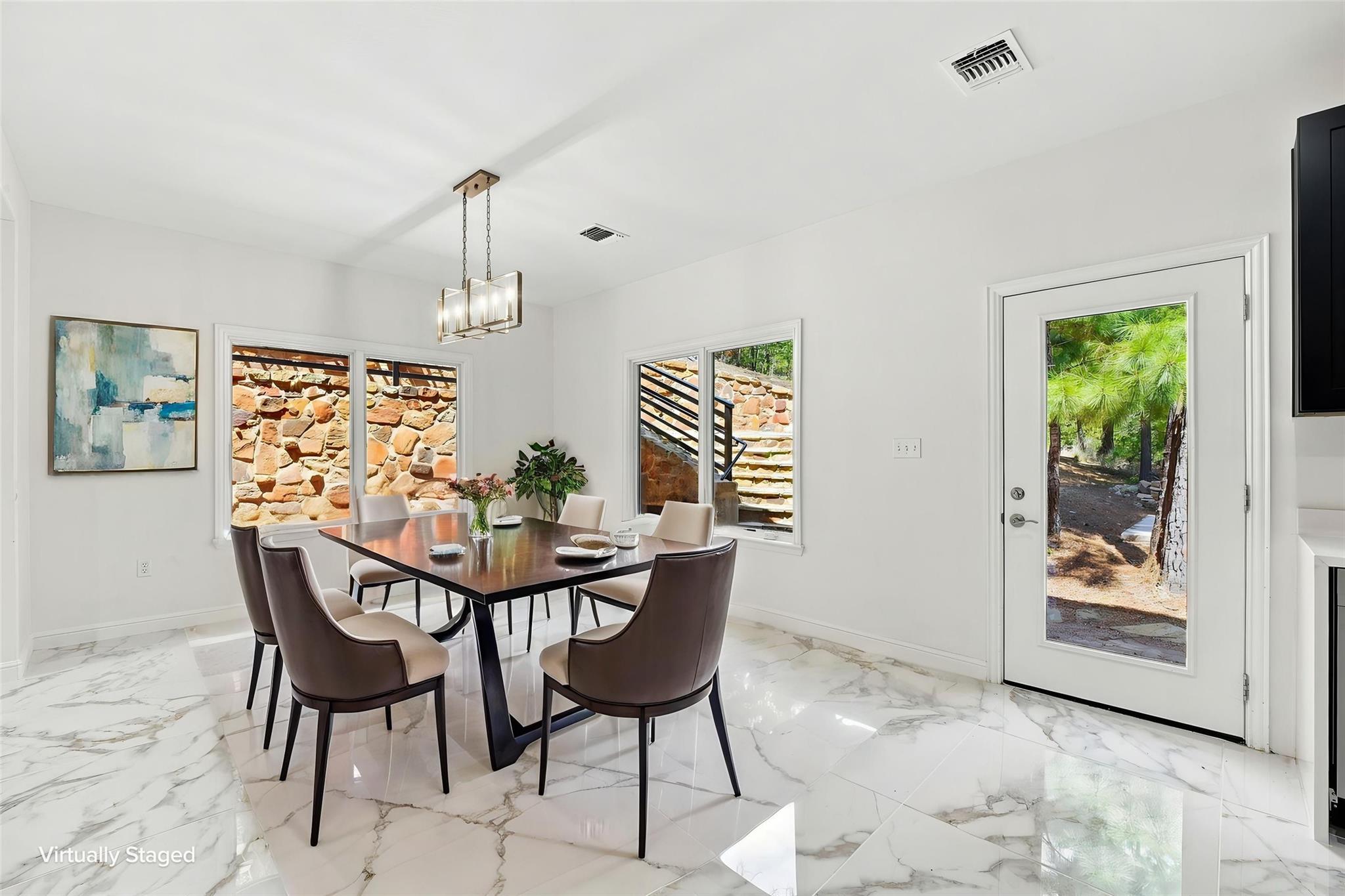 Virtually staged dining room with a dark table, marble-look floors, and windows facing a stone retaining wall.