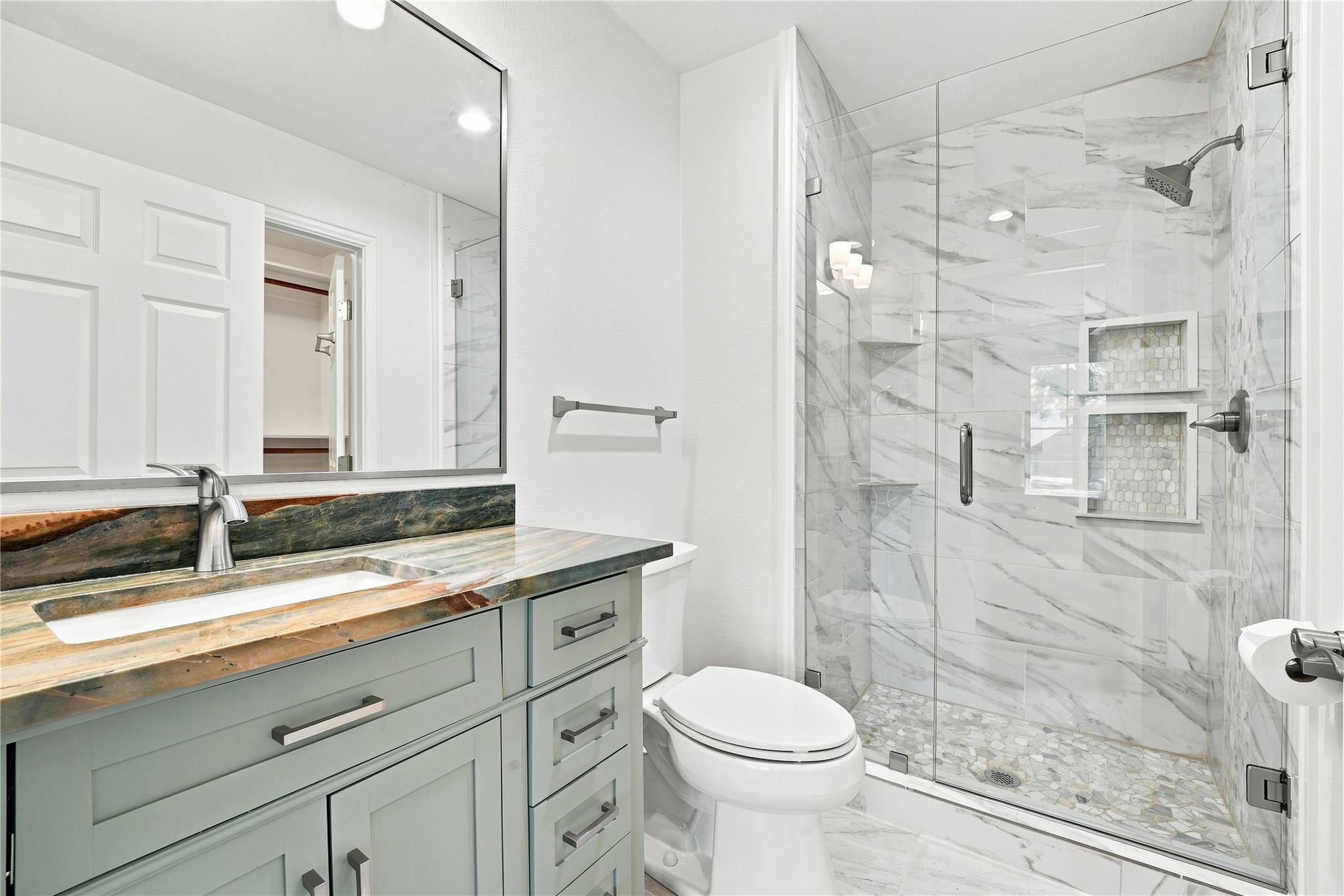 Bathroom with a pale green vanity and glass shower with marble-look tile.