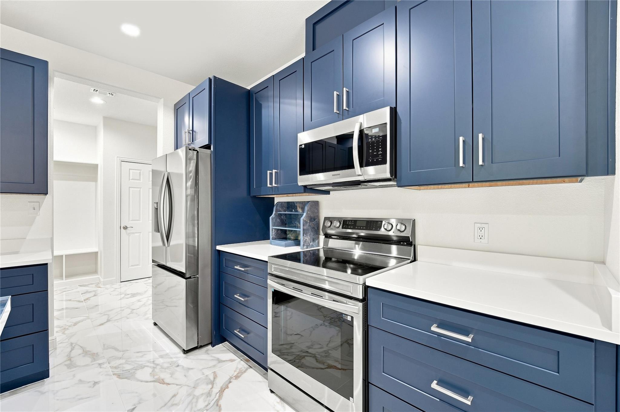 Kitchen with blue cabinets, white countertops, stainless steel appliances, and marble-look tile flooring.
