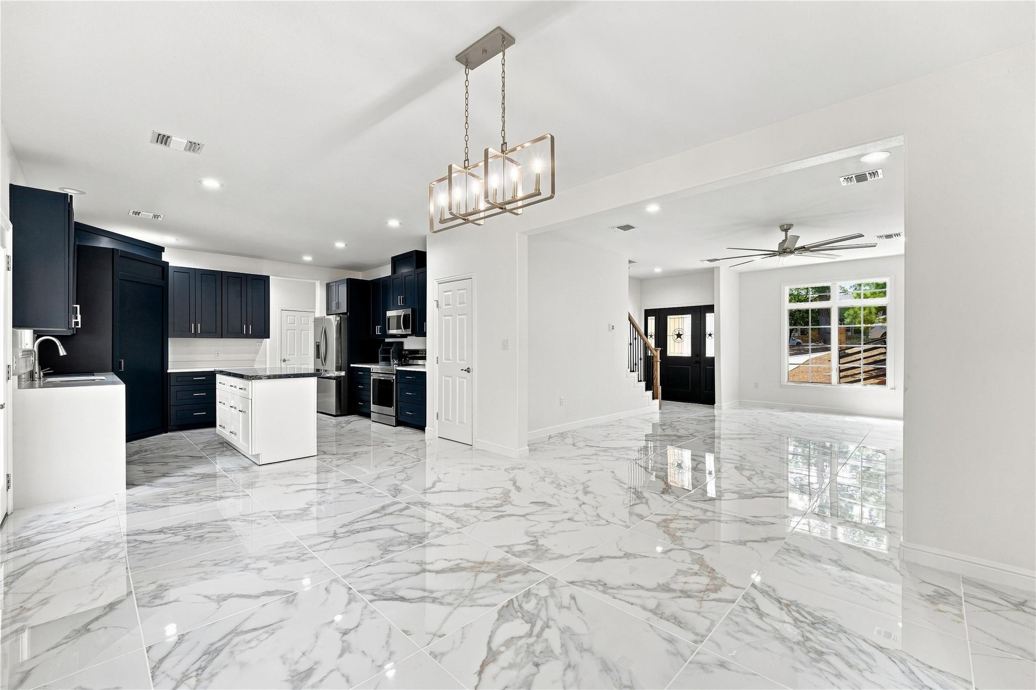 Open-plan kitchen with navy cabinets, white island, and glossy marble-pattern floors.