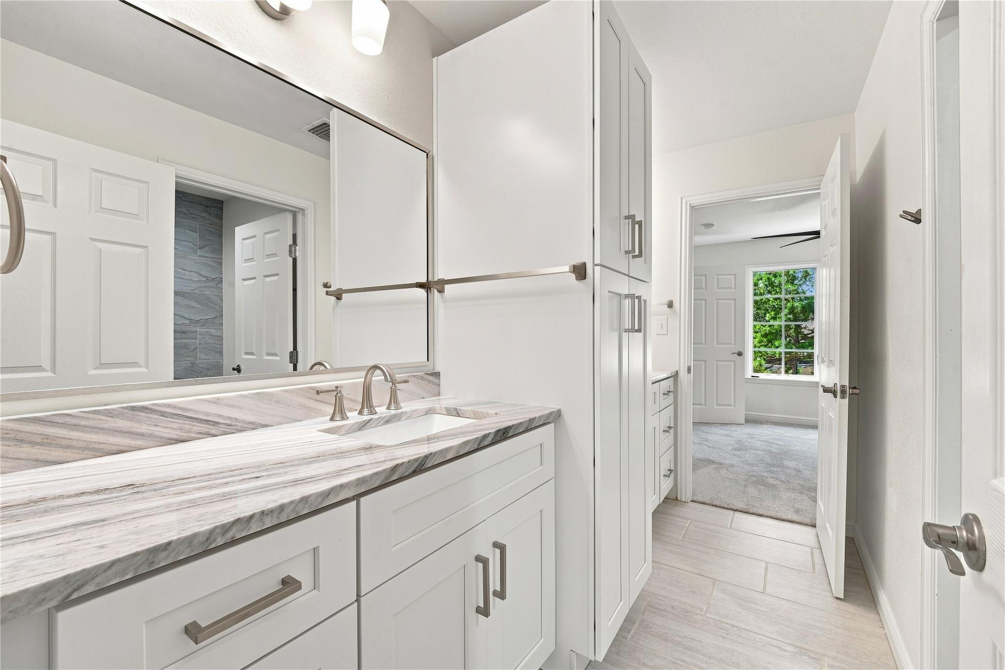 Bathroom vanity with a veined marble counter and tall white cabinets, opening onto a carpeted room.