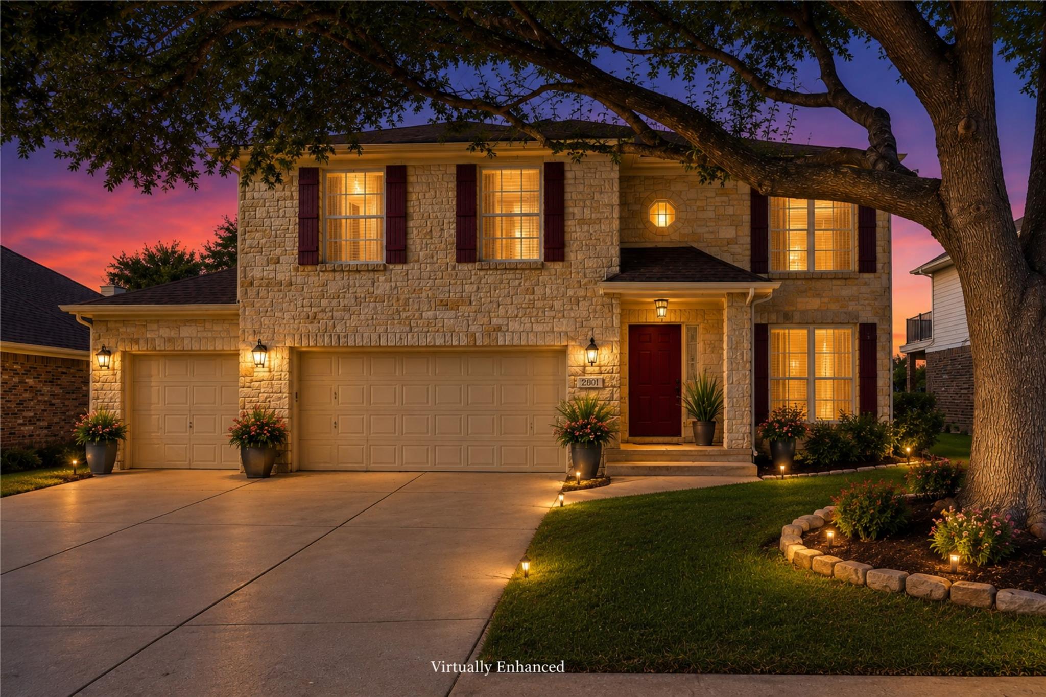 Two-story stone house at dusk, with warmly lit windows, a three-car garage, and a large tree in front.